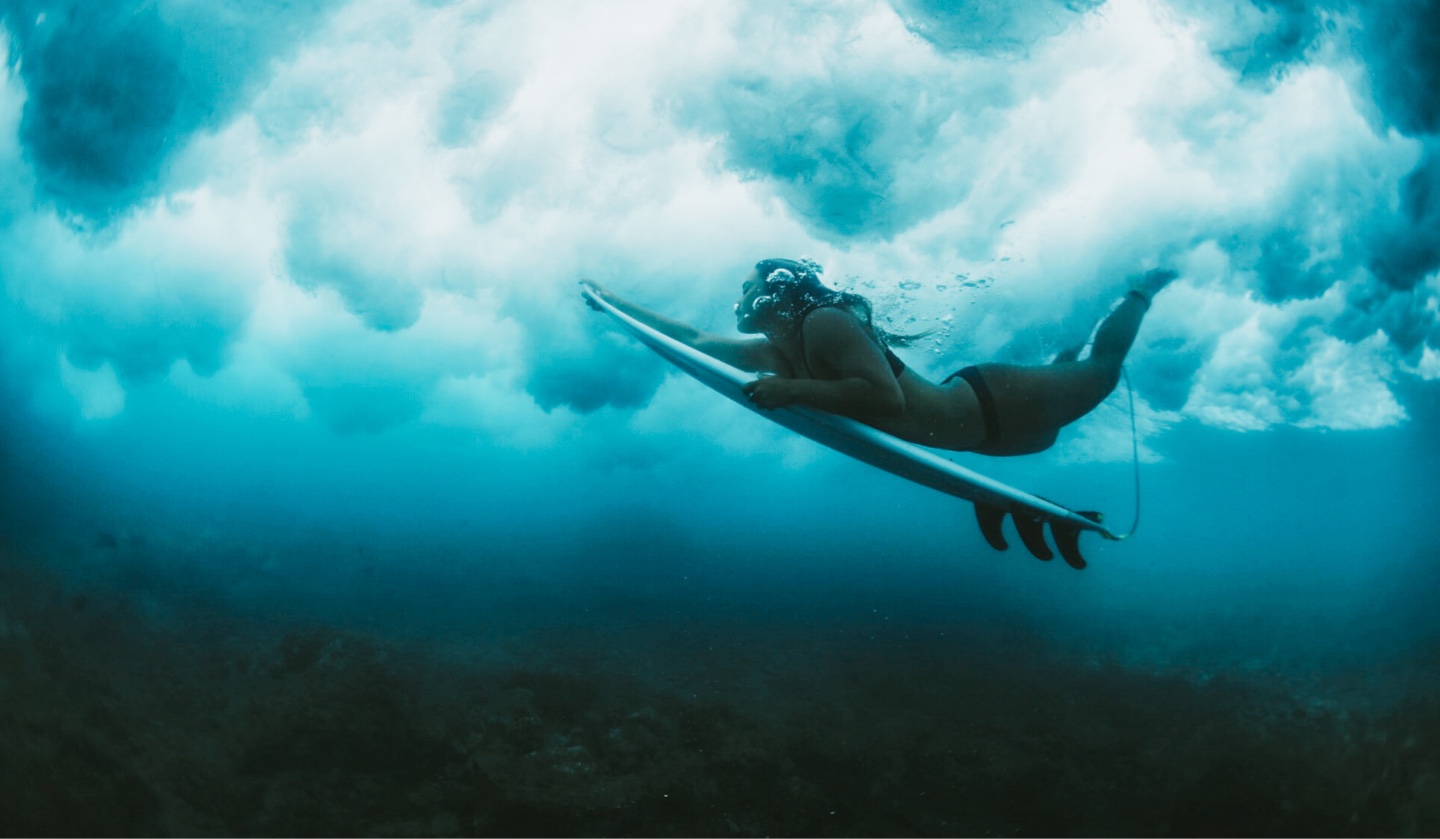 A woman doing a duck dive under a wave in the ocean with a surfboard.