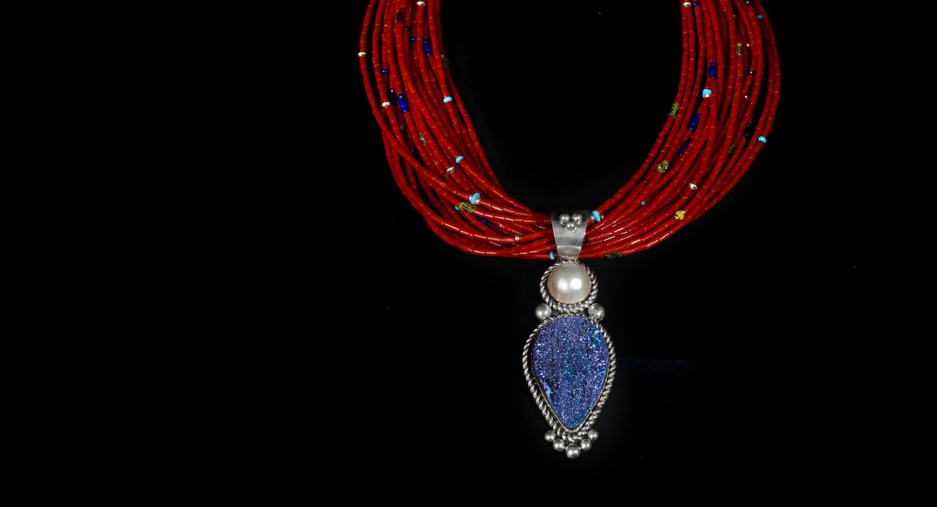 A necklace with red beads and a blue pendant and pearls.