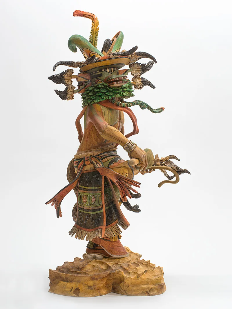A wooden sculpture of a figure with green and orange feathers and robes.