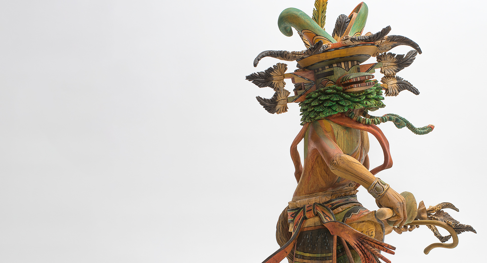 A wooden sculpture of a figure with green and orange feathers and robes.