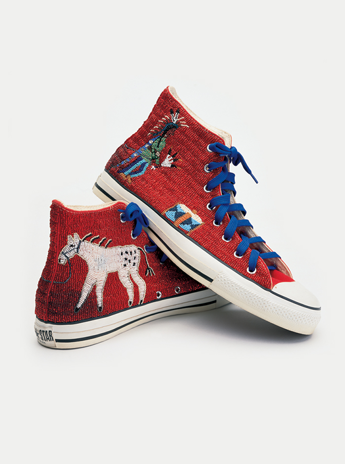 A pair of red beaded Converse sneakers with a design of a Native American and a horse and blue shoestrings.