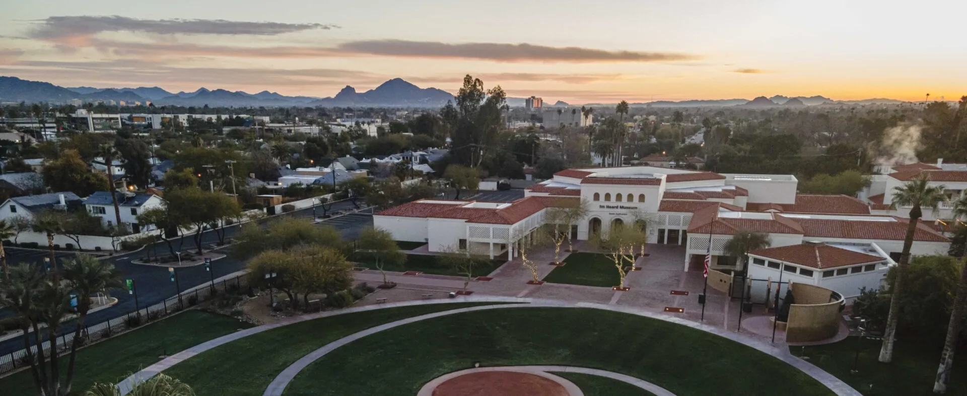 An aerial view of the Heard Museum buildings and courtyard at dawn, featuring a spiral design of pavement and green grass.