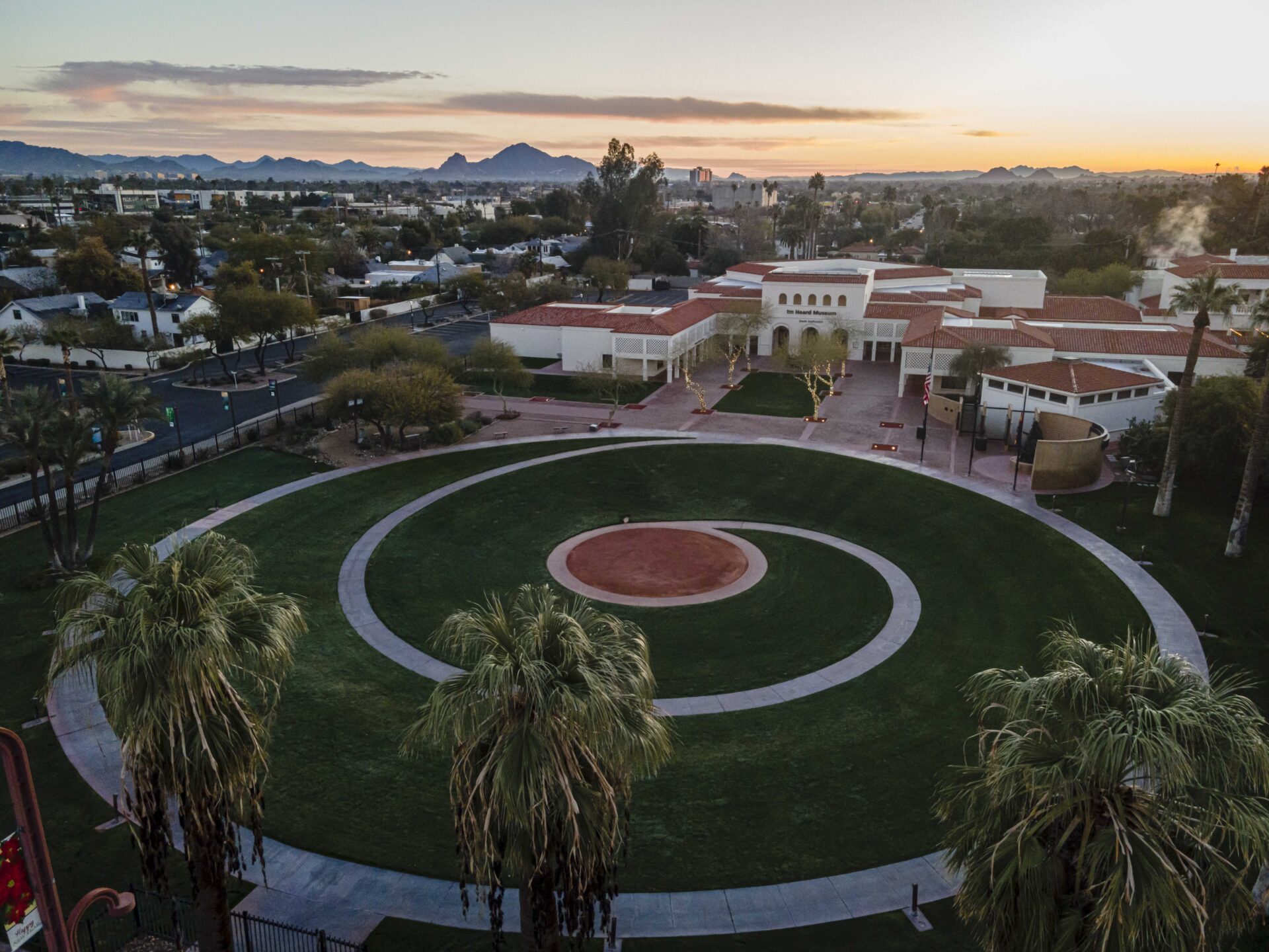 An aerial view of the Heard Museum buildings and courtyard at dawn, featuring a spiral design of pavement and green grass.