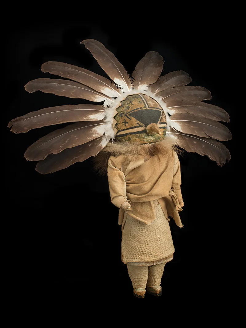 A doll with a feathered headdress on a black background.