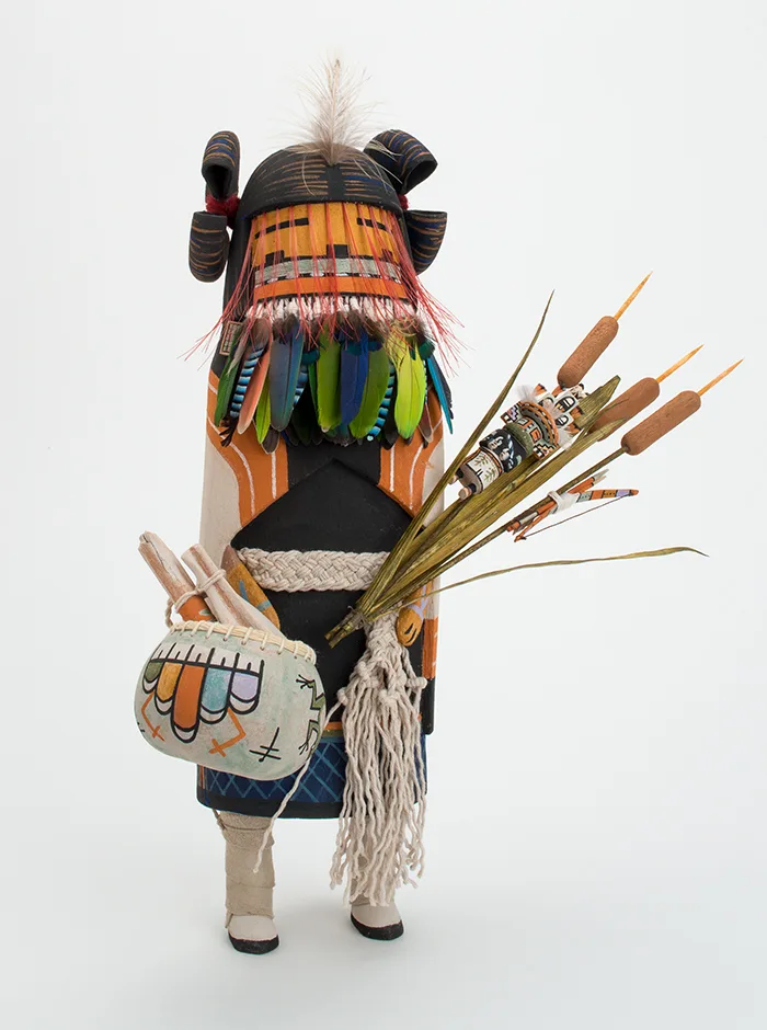 A sculpture with feathers holding a bag and cattails.