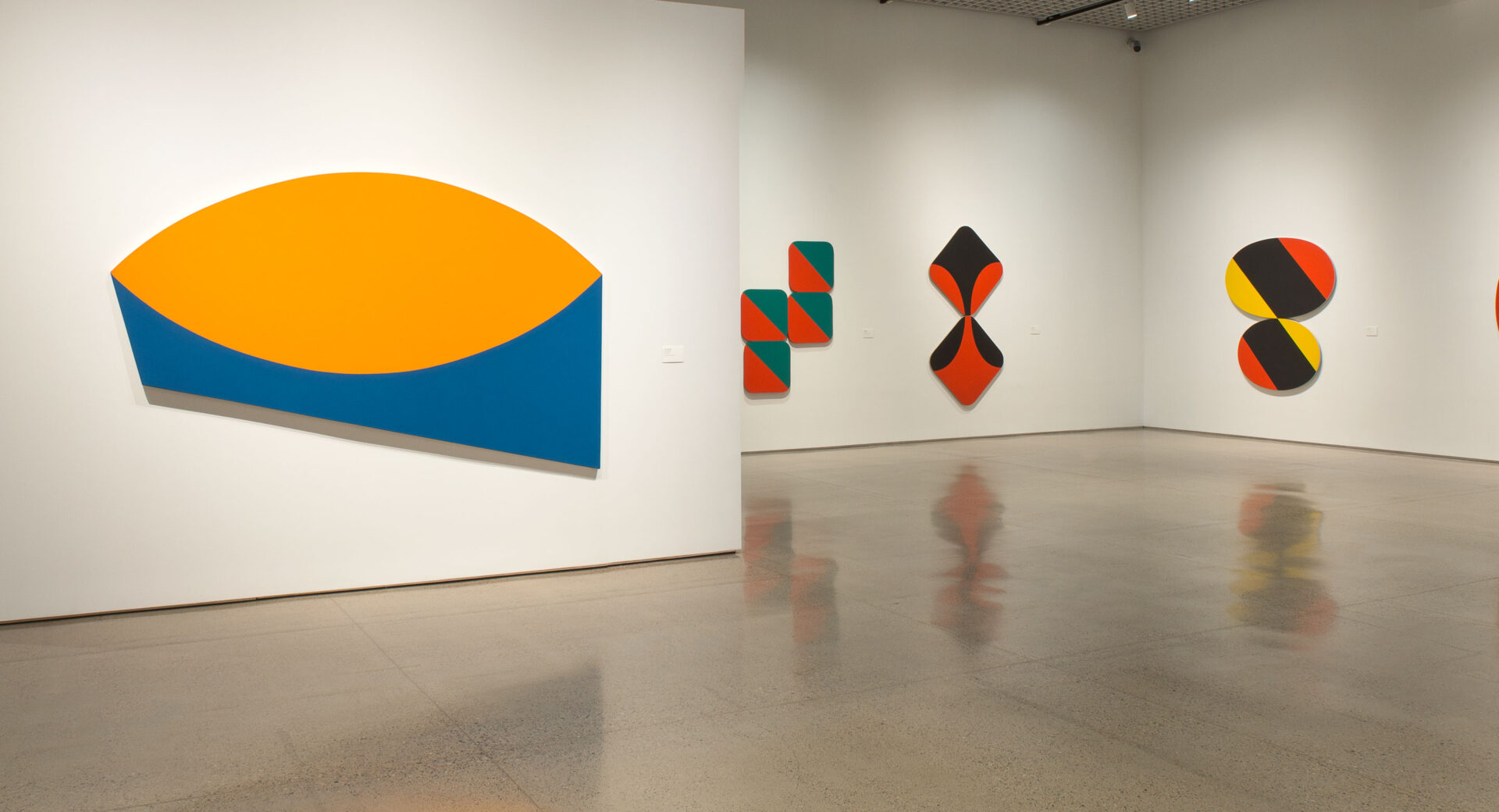A group of colorful, abstract, geometric paintings in an art gallery.