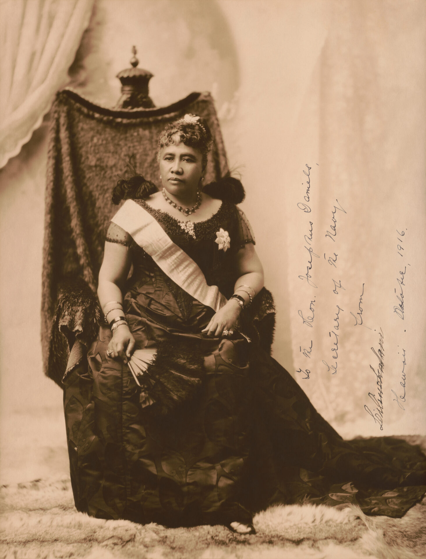 A sepia toned photograph of Queen Liliuokalani sitting on a throne.