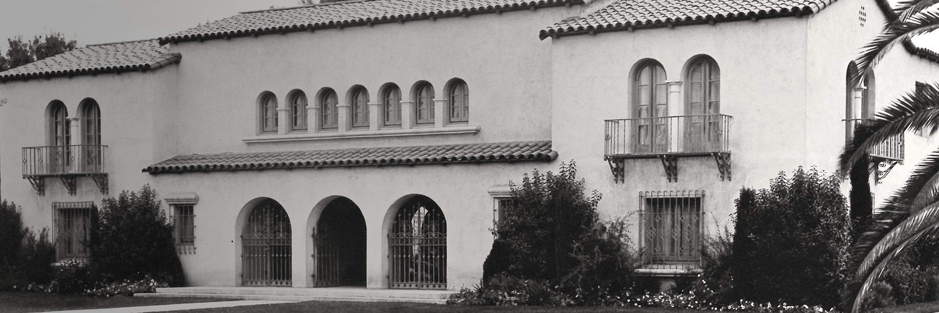 A black and white photo of a house with palm trees.