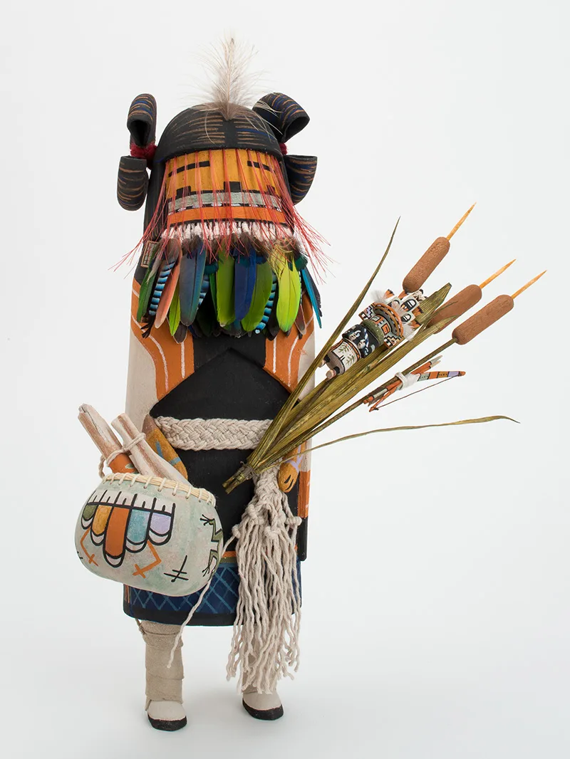 A sculpture with feathers holding a bag and cattails.