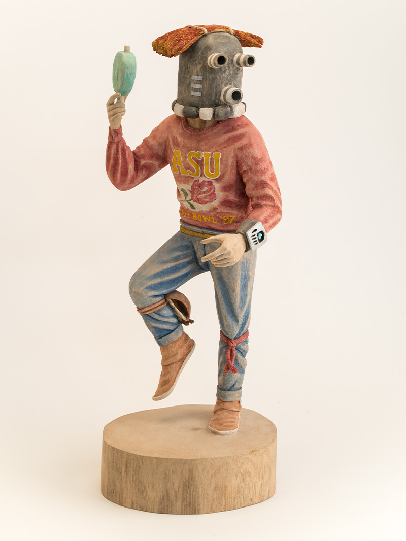 A sculpture of a figure wearing a robot mask and a sweater hold a green object in its hand.