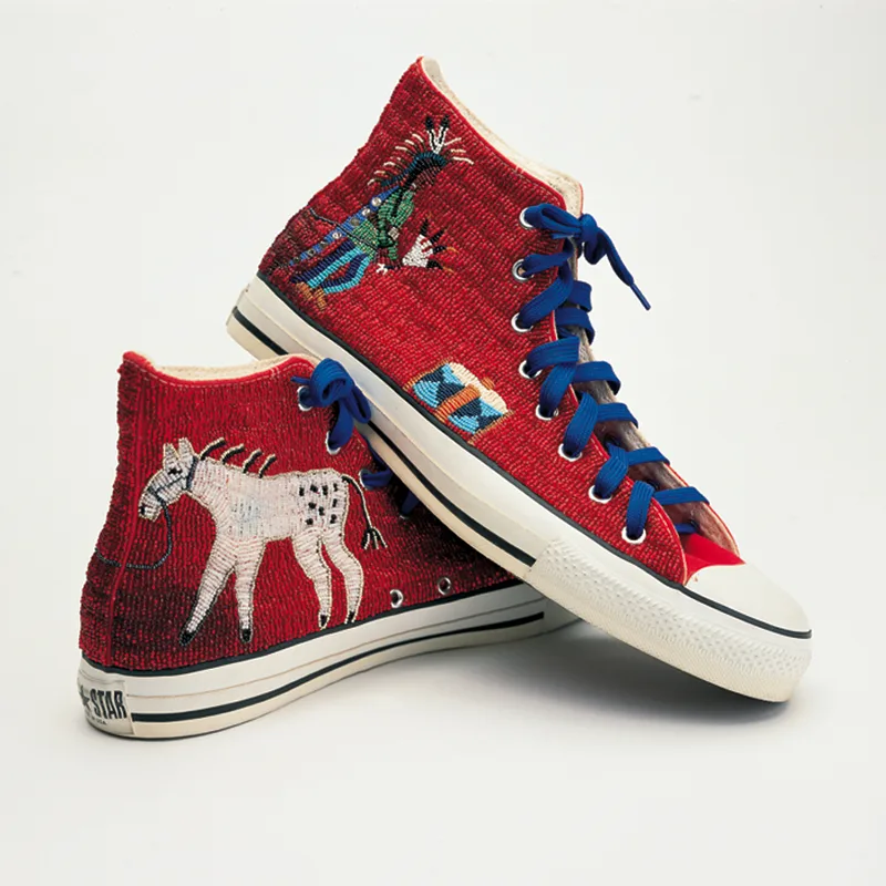 A pair of red beaded Converse sneakers with a design of a Native American and a horse and blue shoestrings.