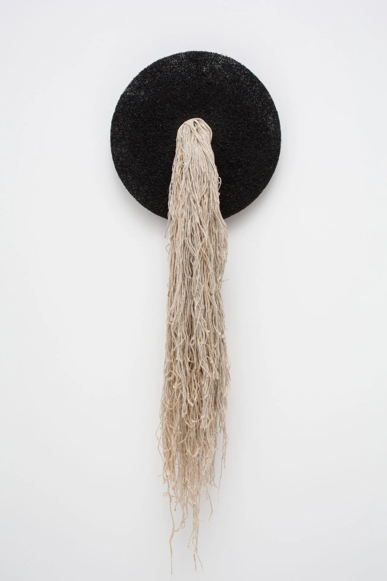 An artwork hanging on a wall with a black circle and white string hanging from it.