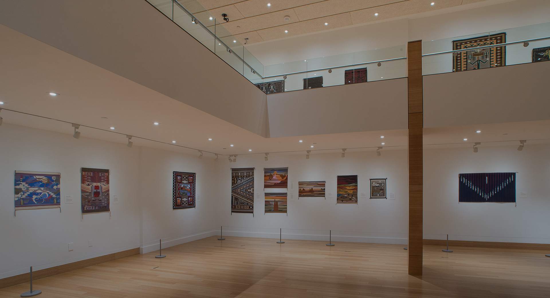 A two story gallery with paintings on the walls and a wooden floor.