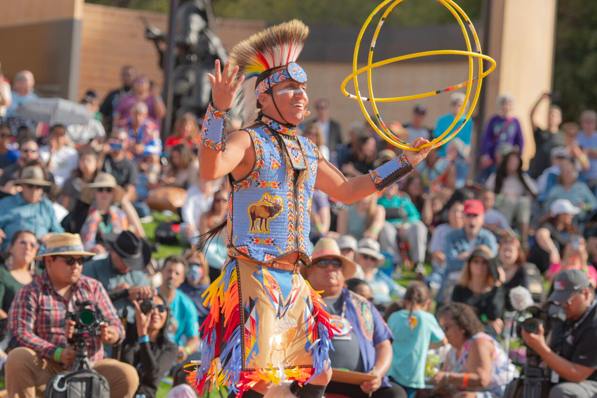 A Native dancer with a hoop in front of a crowd.