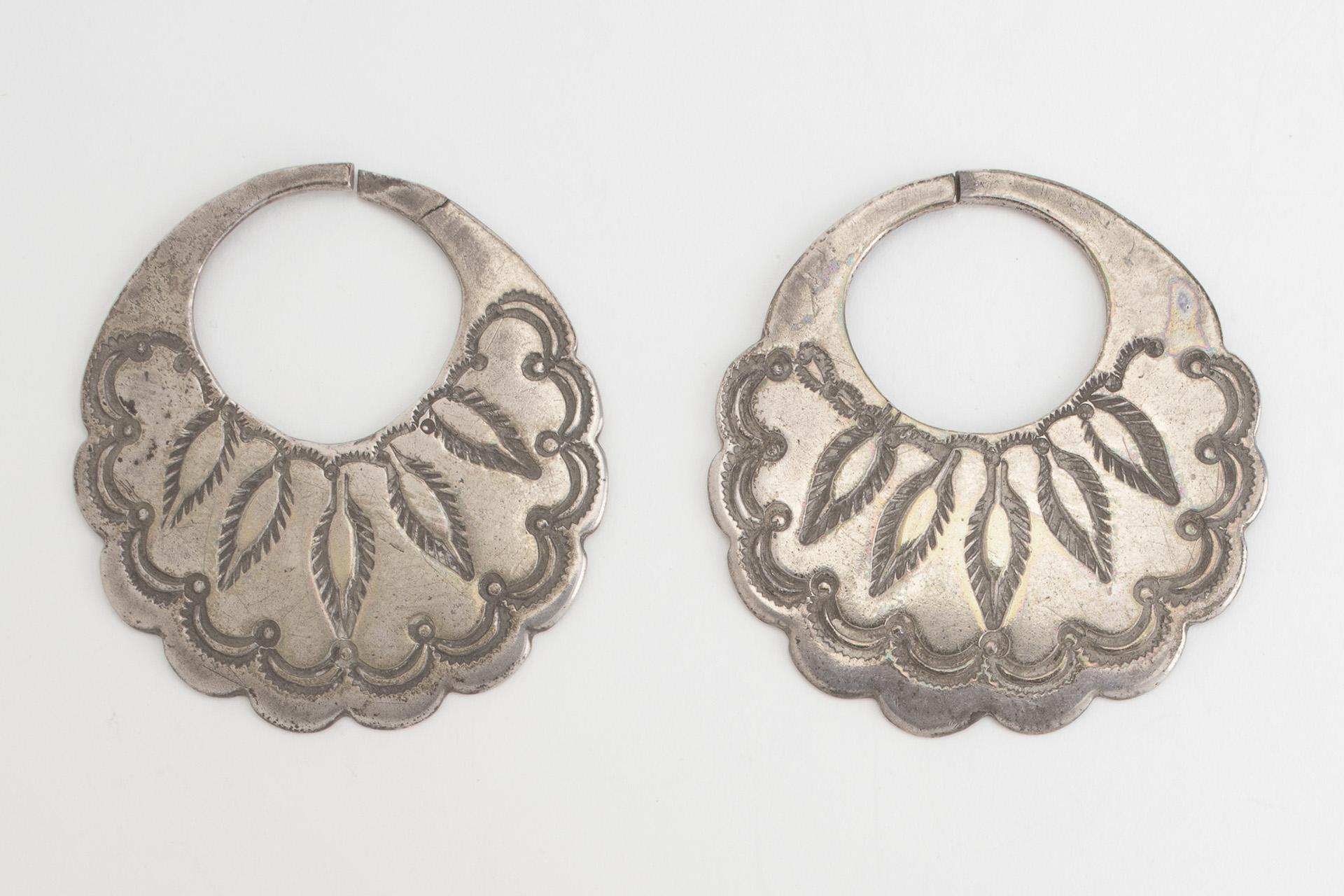 A pair of silver earrings with an ornate design on them.