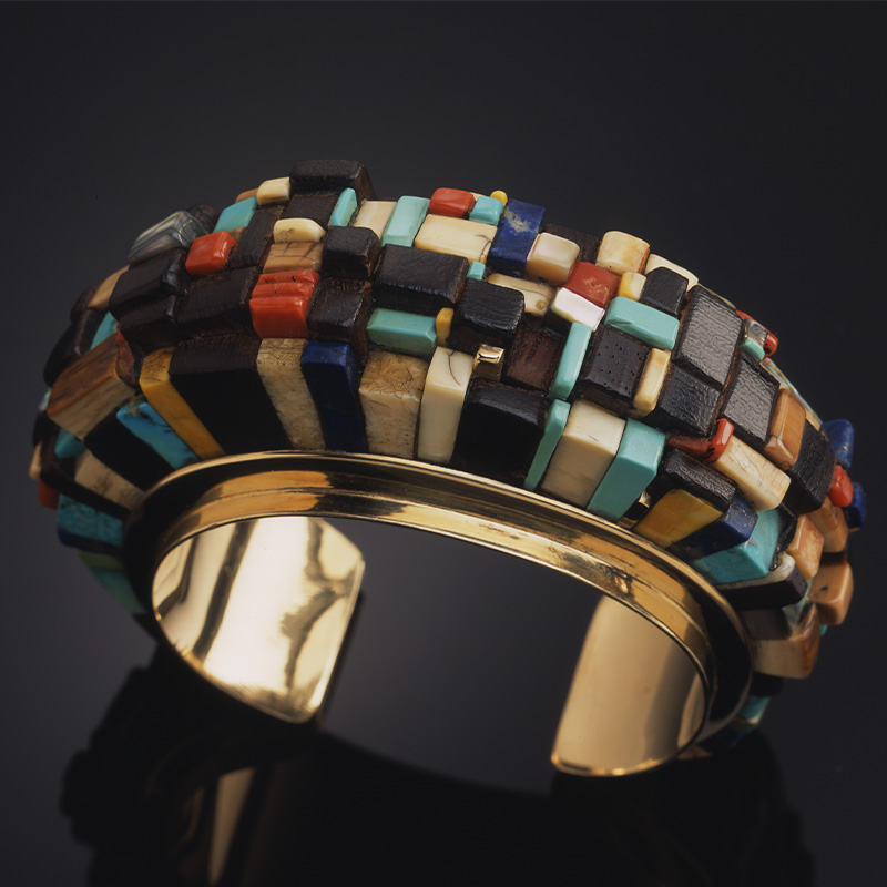 A colorful gold cuff bracelet with multi colored stones.