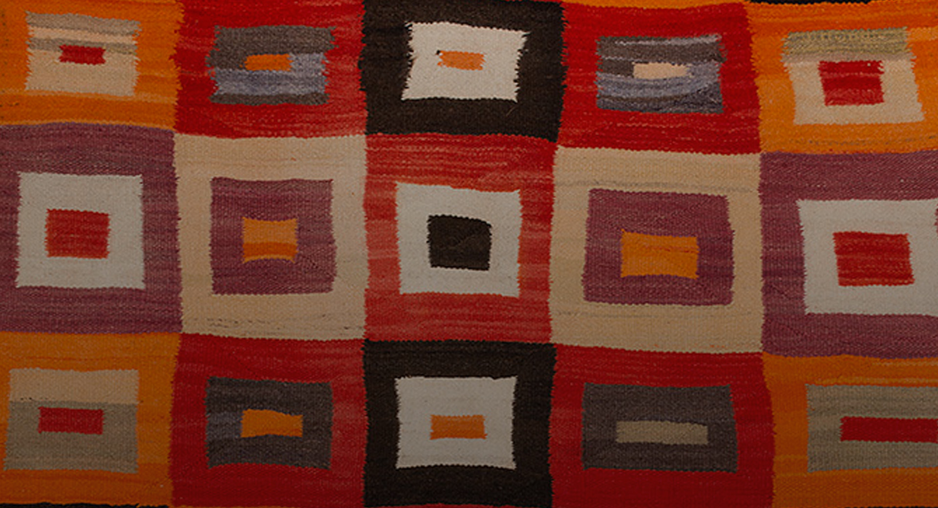 A Navajo textile with different sized squares on it in shades of red, orange, black and white.