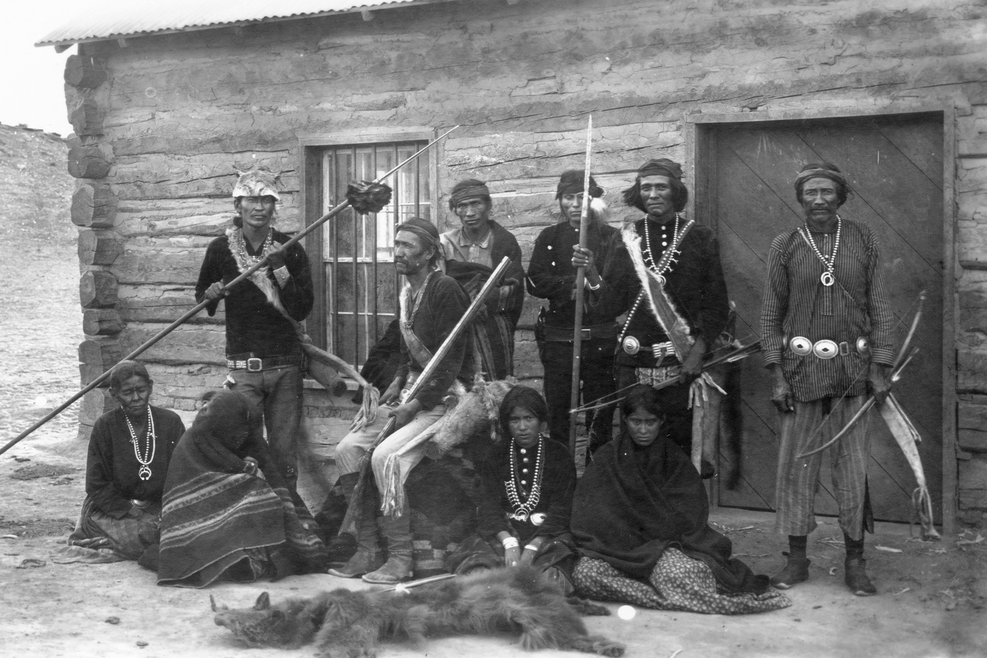 A black and white photo of a group of Native people posing in front of a house.