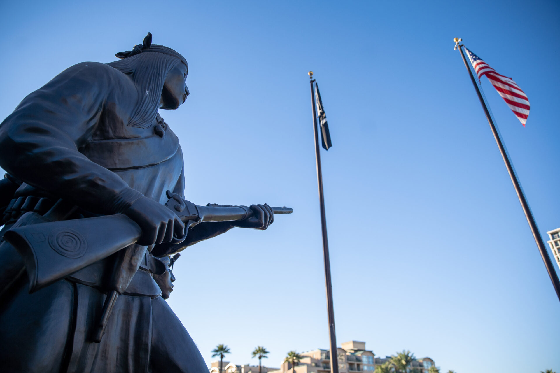 A sculpture of a Native man holding a rifle next to pole flags.