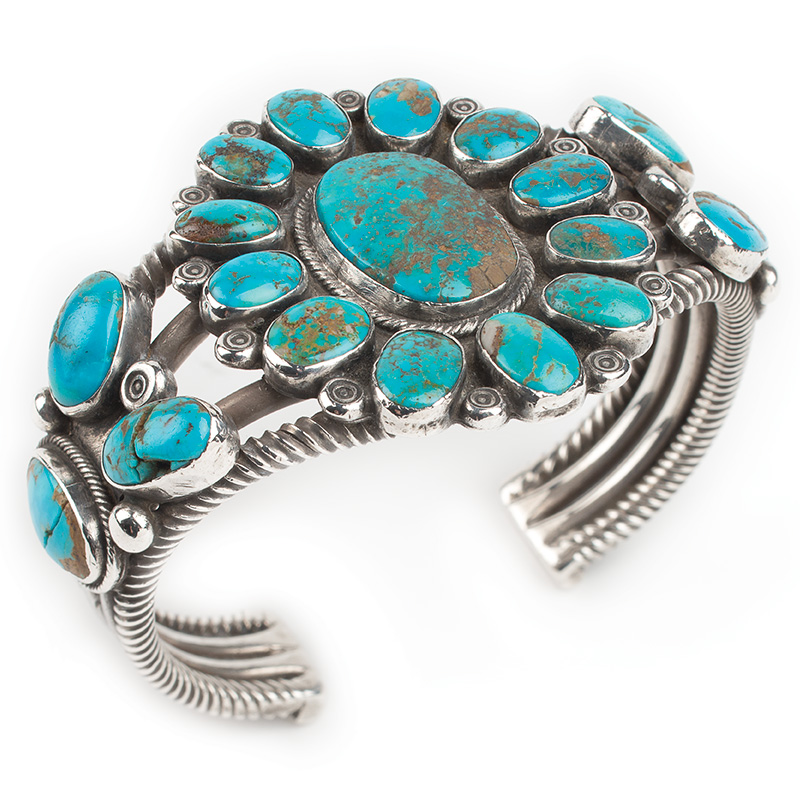 A silver cuff bracelet with turquoise stones in a flower design.