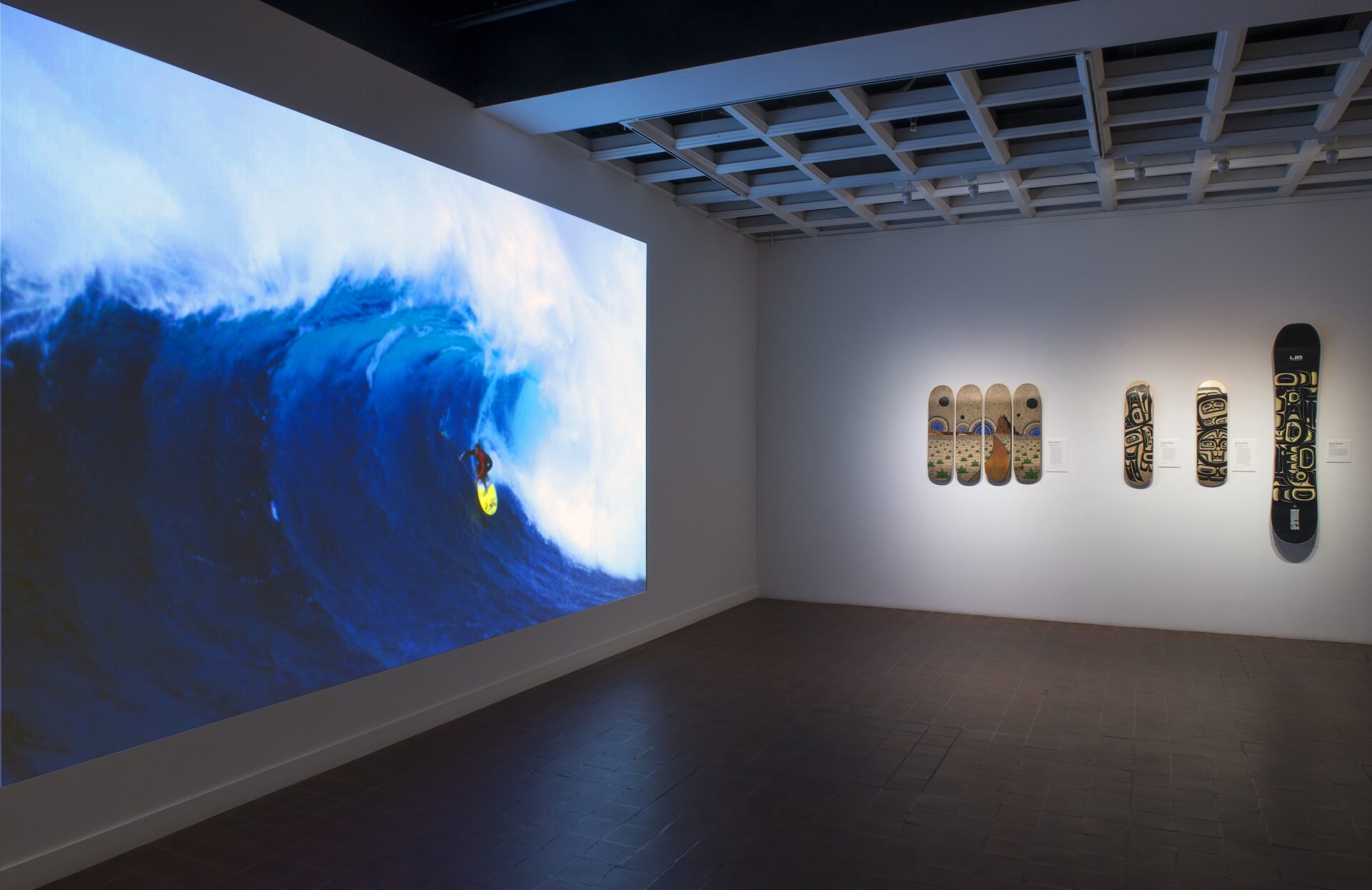 A room with several surfboards on the wall and a digital still of a surfer on a wave.