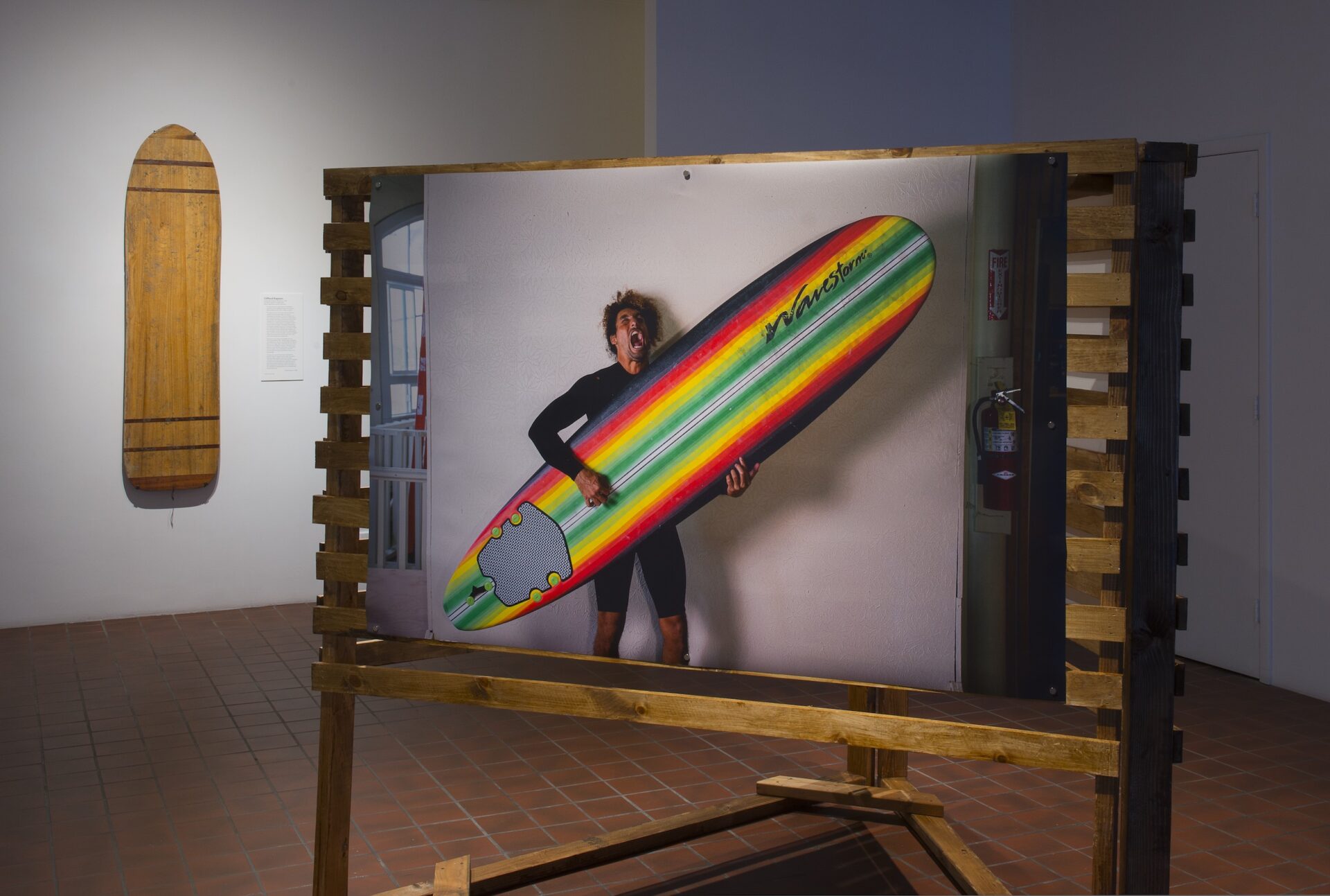 A photo of a man holding a colorful surfboard on an easel.