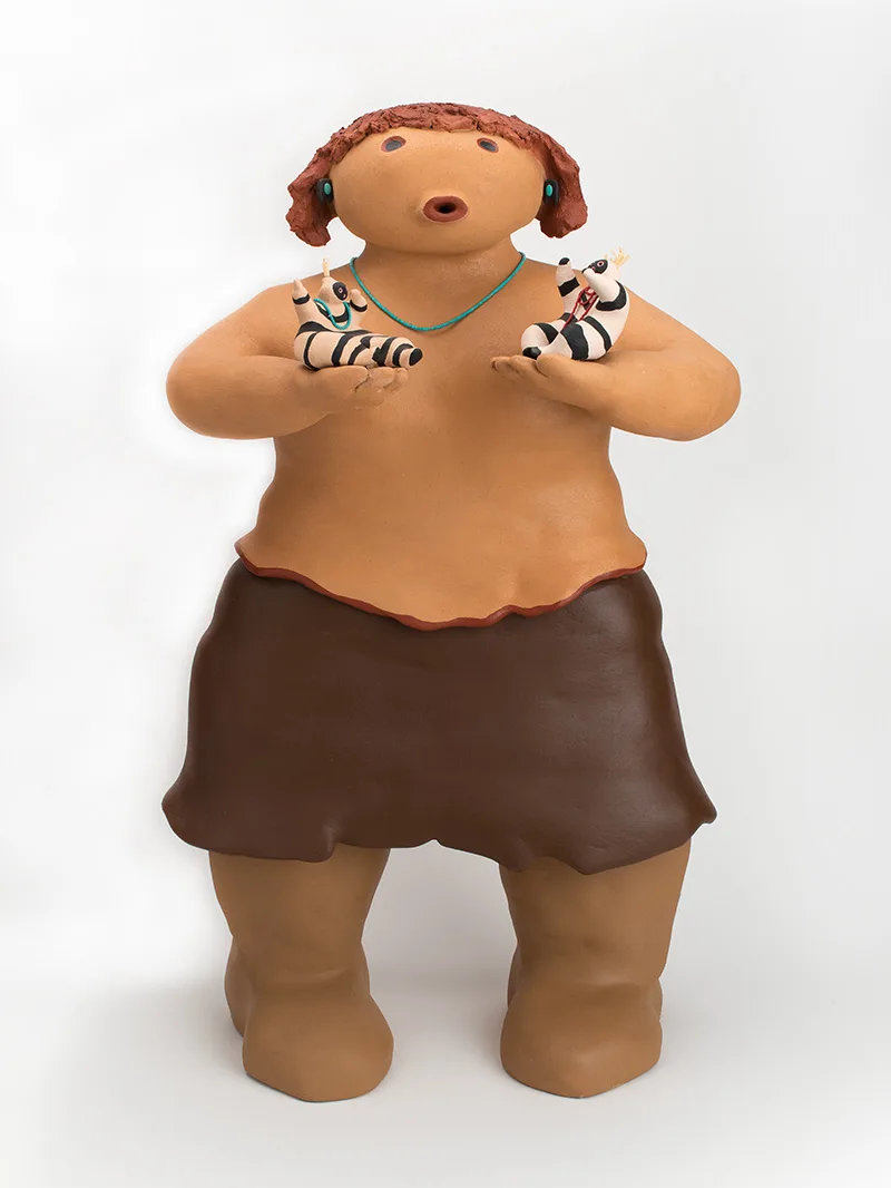 A clay sculpture of a woman holding tiny black and white striped figures in her hands.