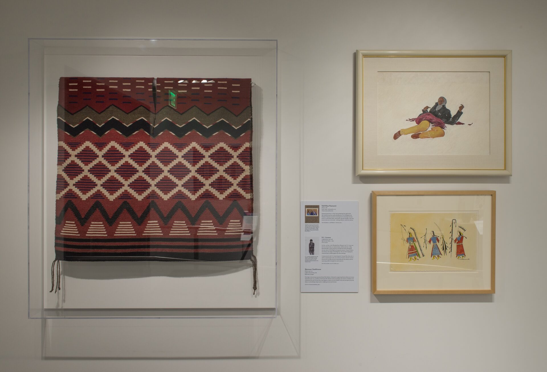 A display of Native paintings and a textile on a gallery wall.