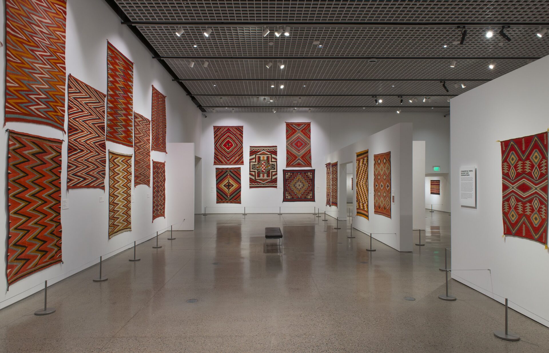 A gallery space with a lot of textiles designed in shades of red on display on the walls.