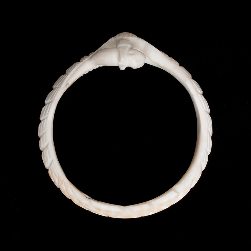 A white carved bracelet with a bird eating a snake on it seen from overhead.