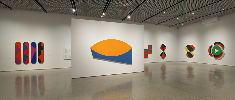 A group of colorful paintings with geometric shapes in an art gallery.