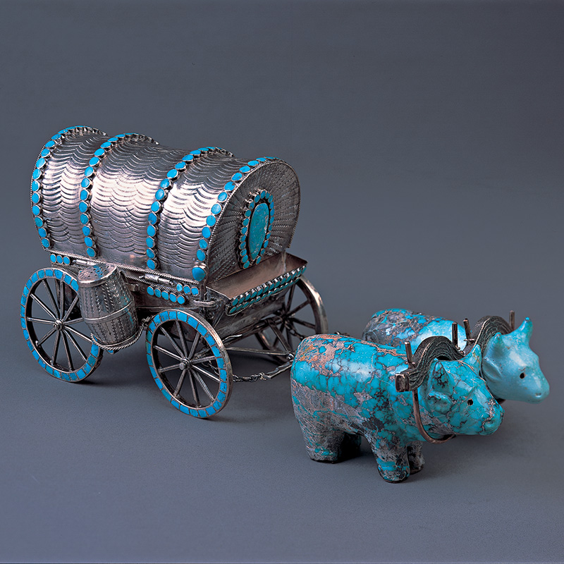 A turquoise and silver figurine of a covered wagon and two oxen.