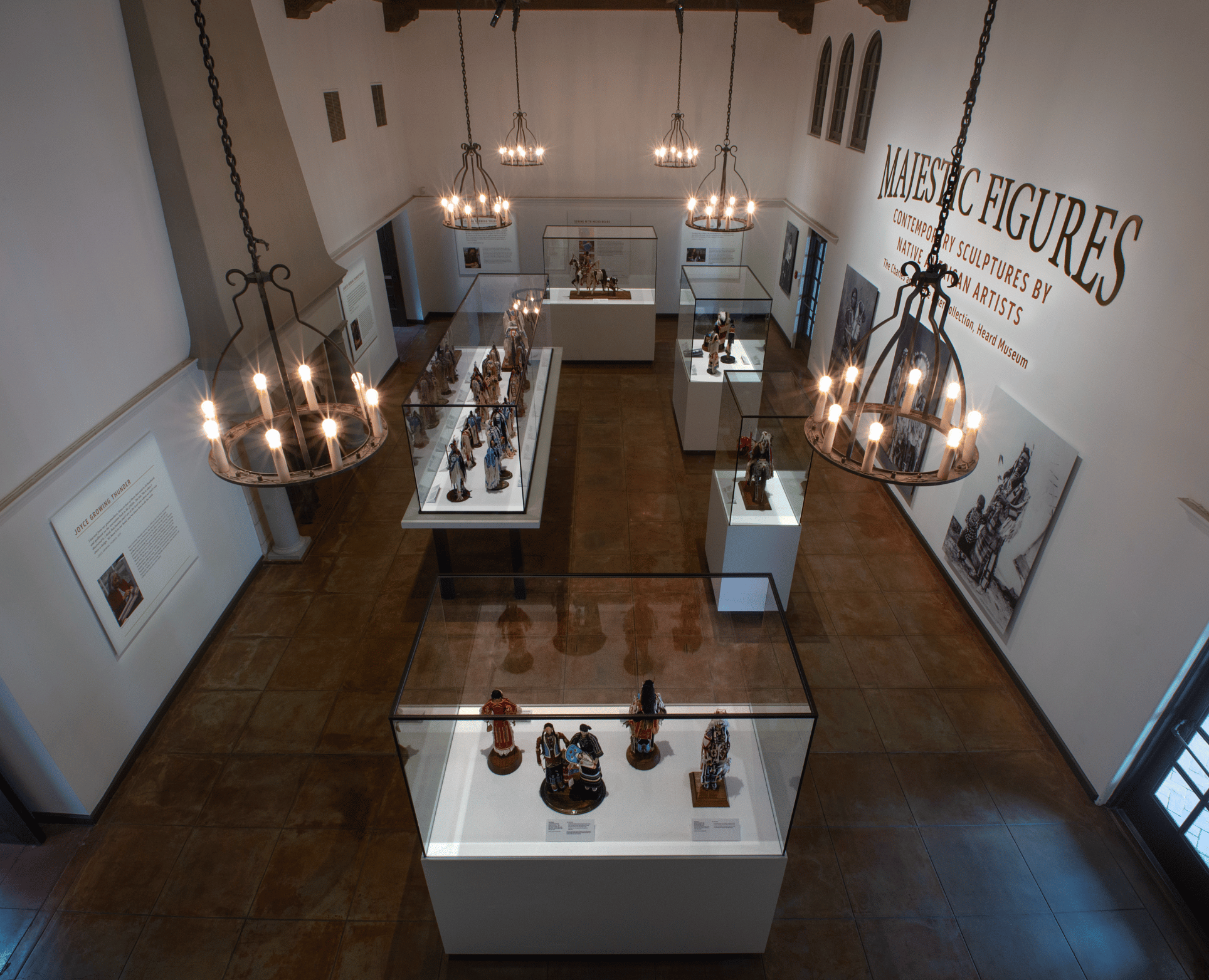 A museum exhibit room featuring multiple lit chandeliers and display cases containing various sculptures. The wall displays the text "Majestic Figures.