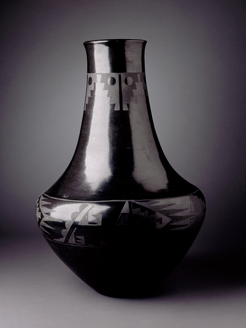 A black jar with a high neck and designs on it.