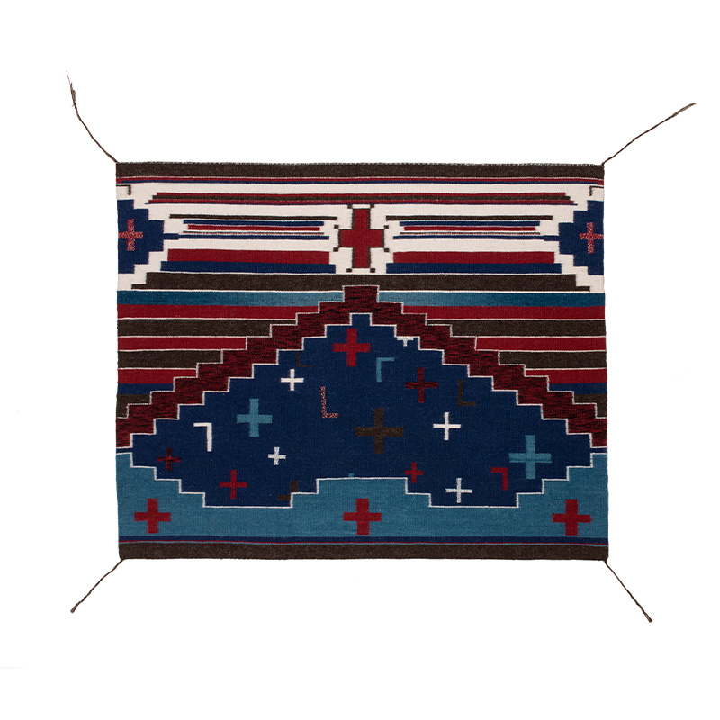 A blue and red Diné blanket with a cross in the middle.
