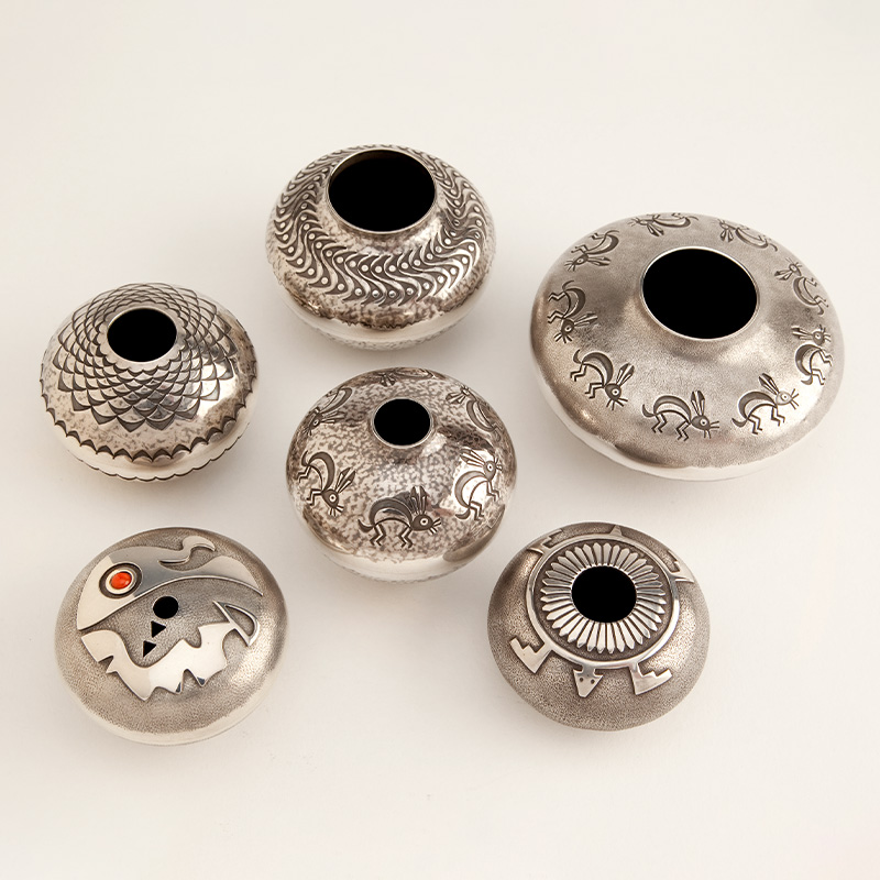 A group of silver seed pots with designs on them.