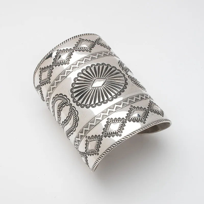 A silver cuff bracelet with designs on it.