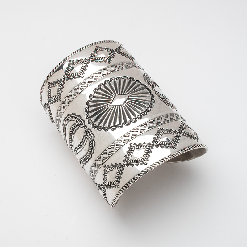 A silver cuff bracelet with designs on it.