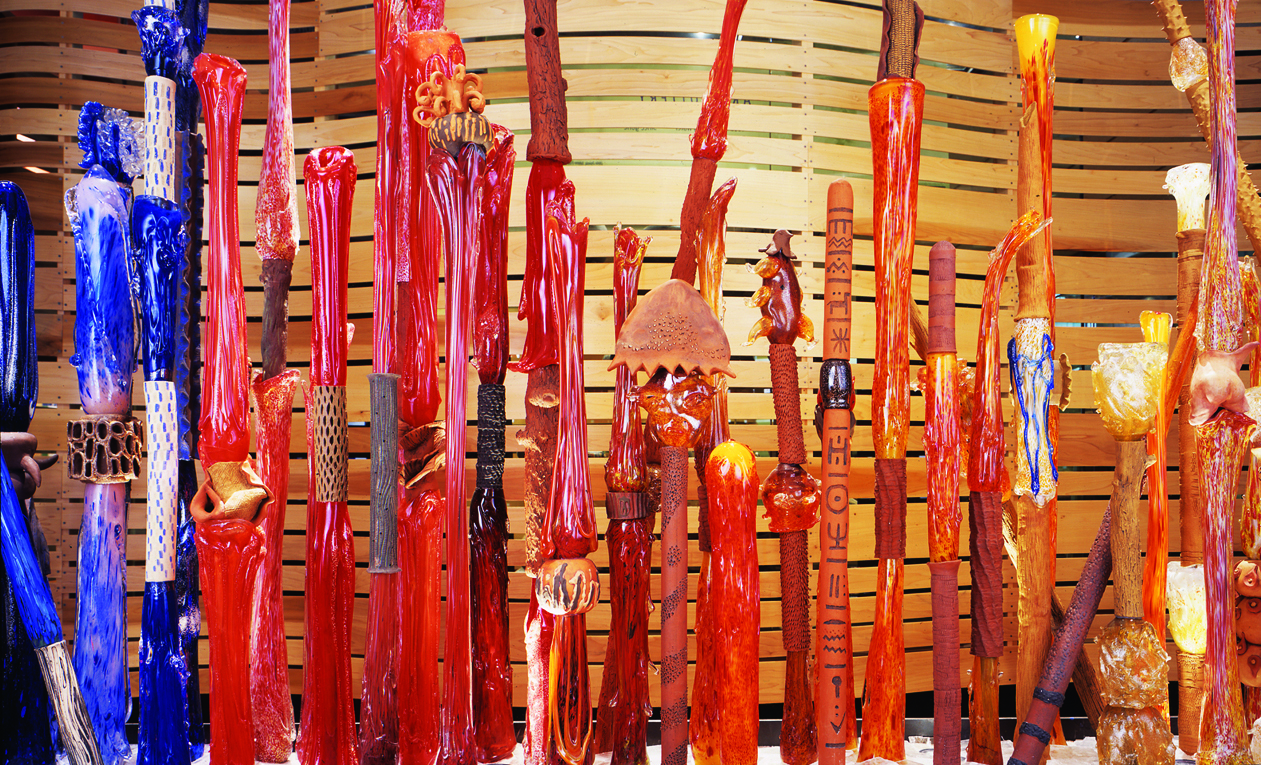 A display of colorful glass sticks known as the Art Fence in front of a wooden wall.