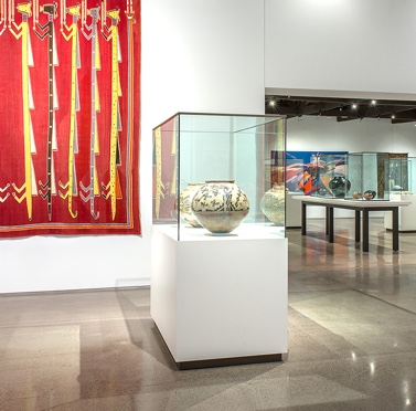 A museum gallery with pottery on display and a textile hanging on the wall.