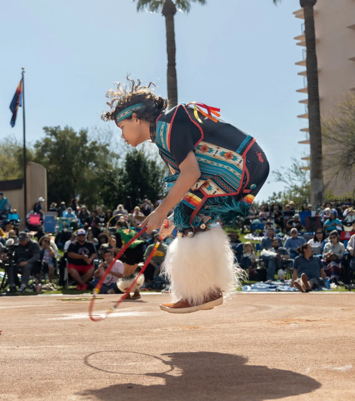 A youth hoop dancer jumping midair through a hoop during a performance.