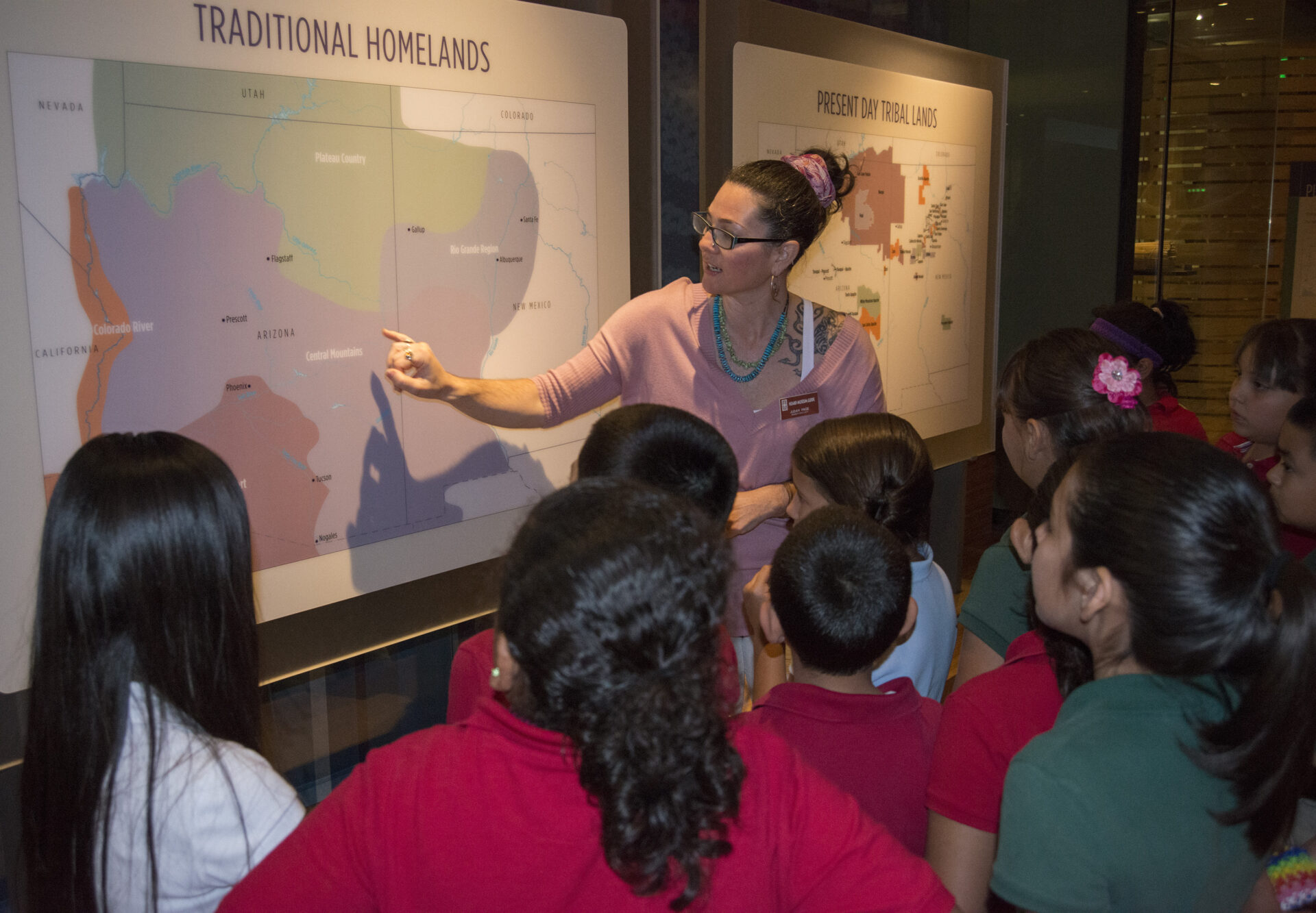 A woman in a red shirt pointing to a map and talking to a group of children.