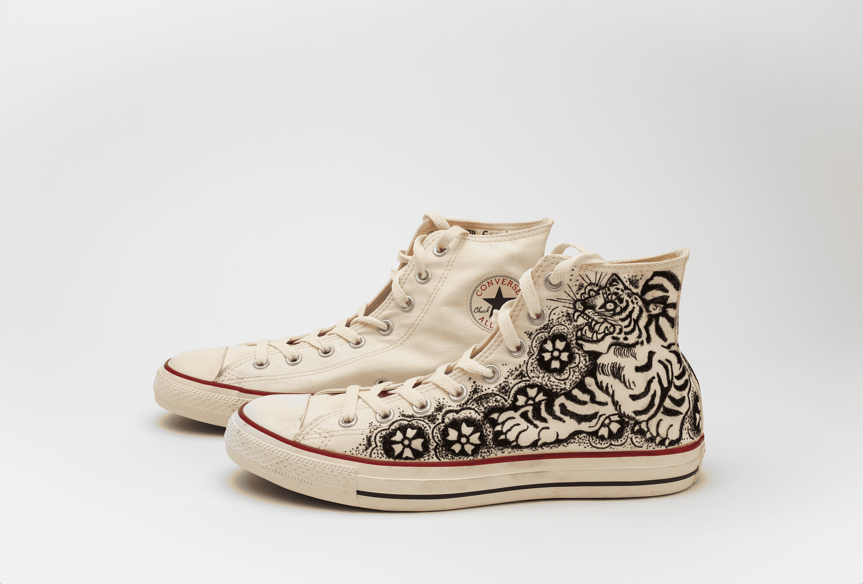 A pair of high-top sneakers with an intricate tiger and floral design embroidered on the side.