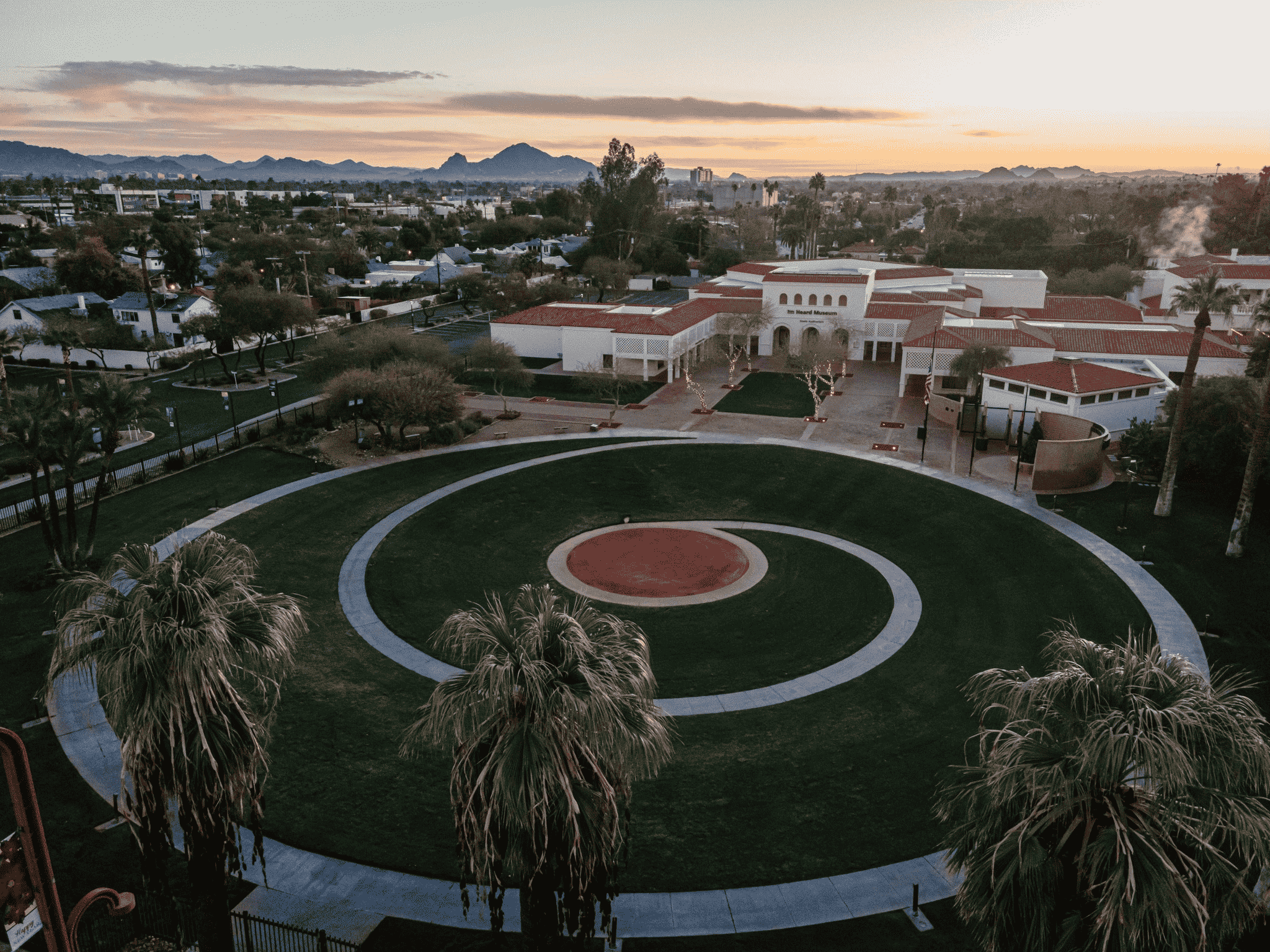 An aerial view of a circular lawn with palm trees and a building in the background.