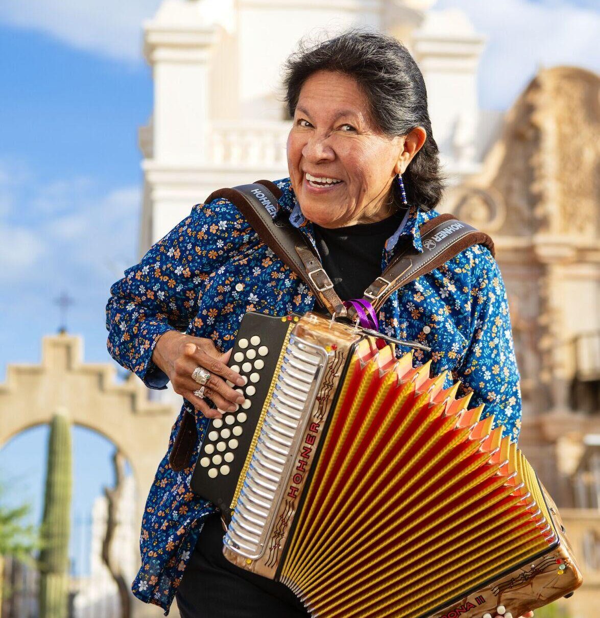 A woman playing an accordion in front of a church.