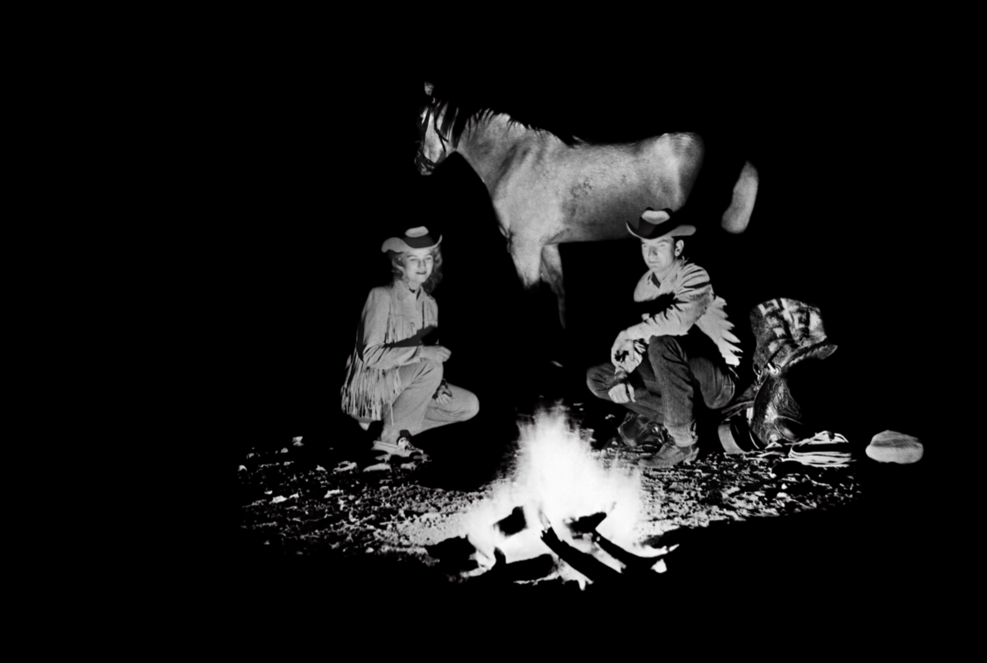 Two people in western attire sit by a campfire with a standing horse in the background, all against a dark backdrop.