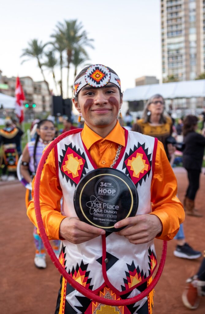 A young man in a native outfit holding a plaque.