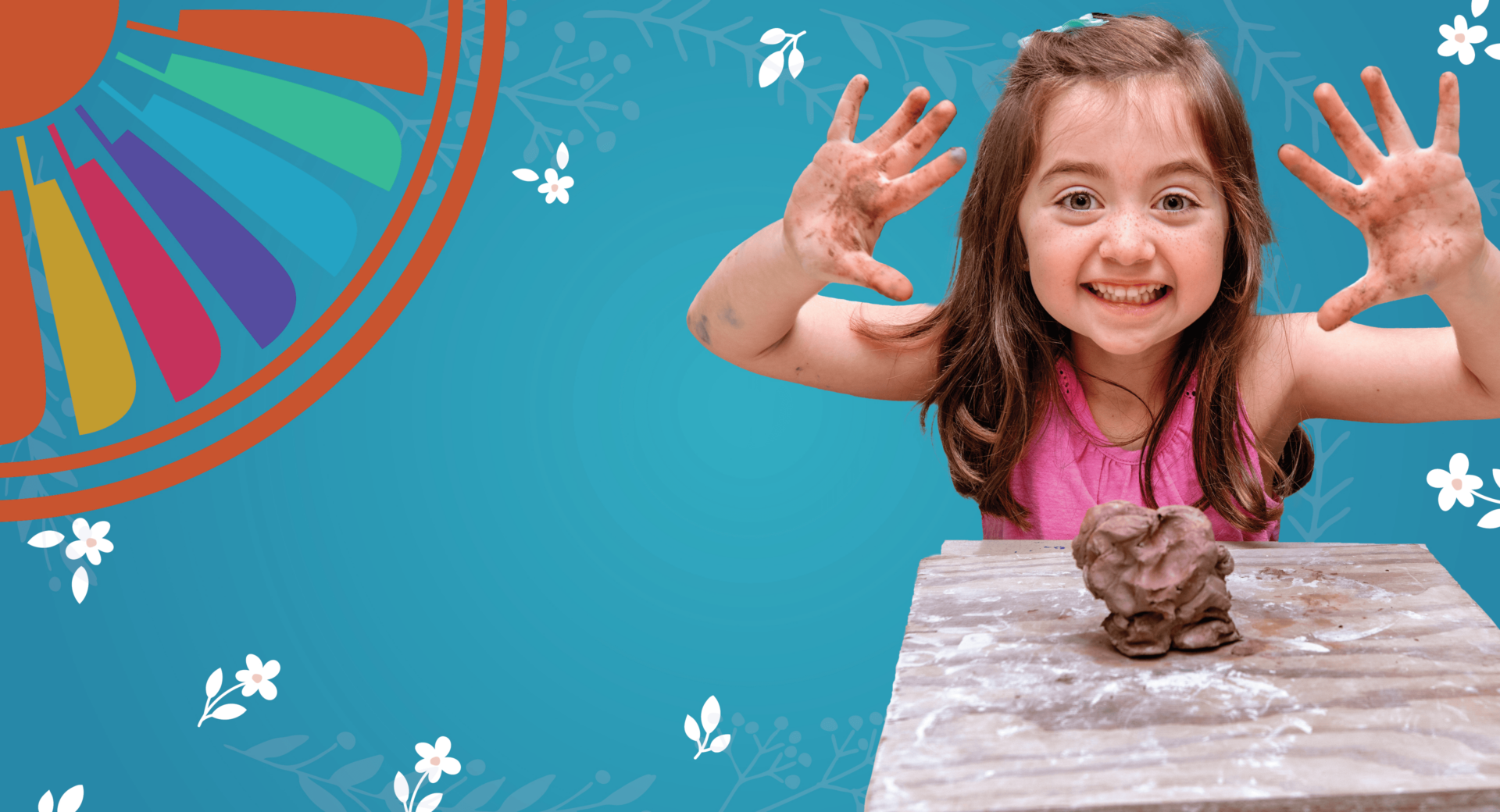 A cheerful young girl showing her paint-covered hands with a lump of brown clay on the table in front of her.