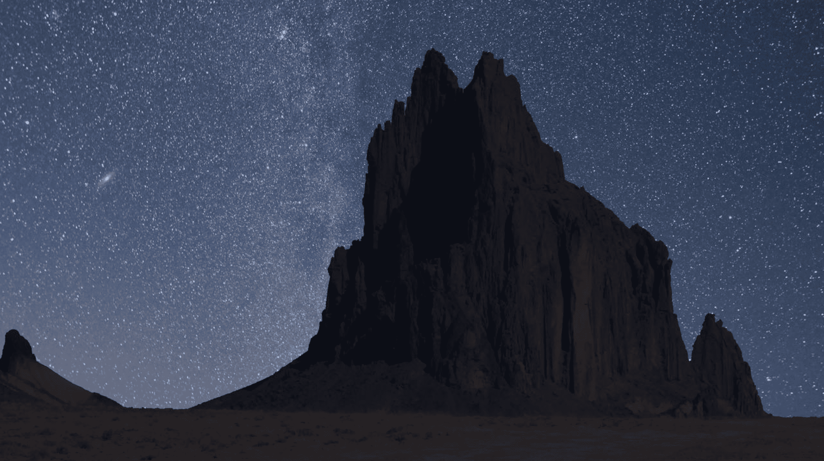Starry night sky over a silhouetted mountainous landscape.