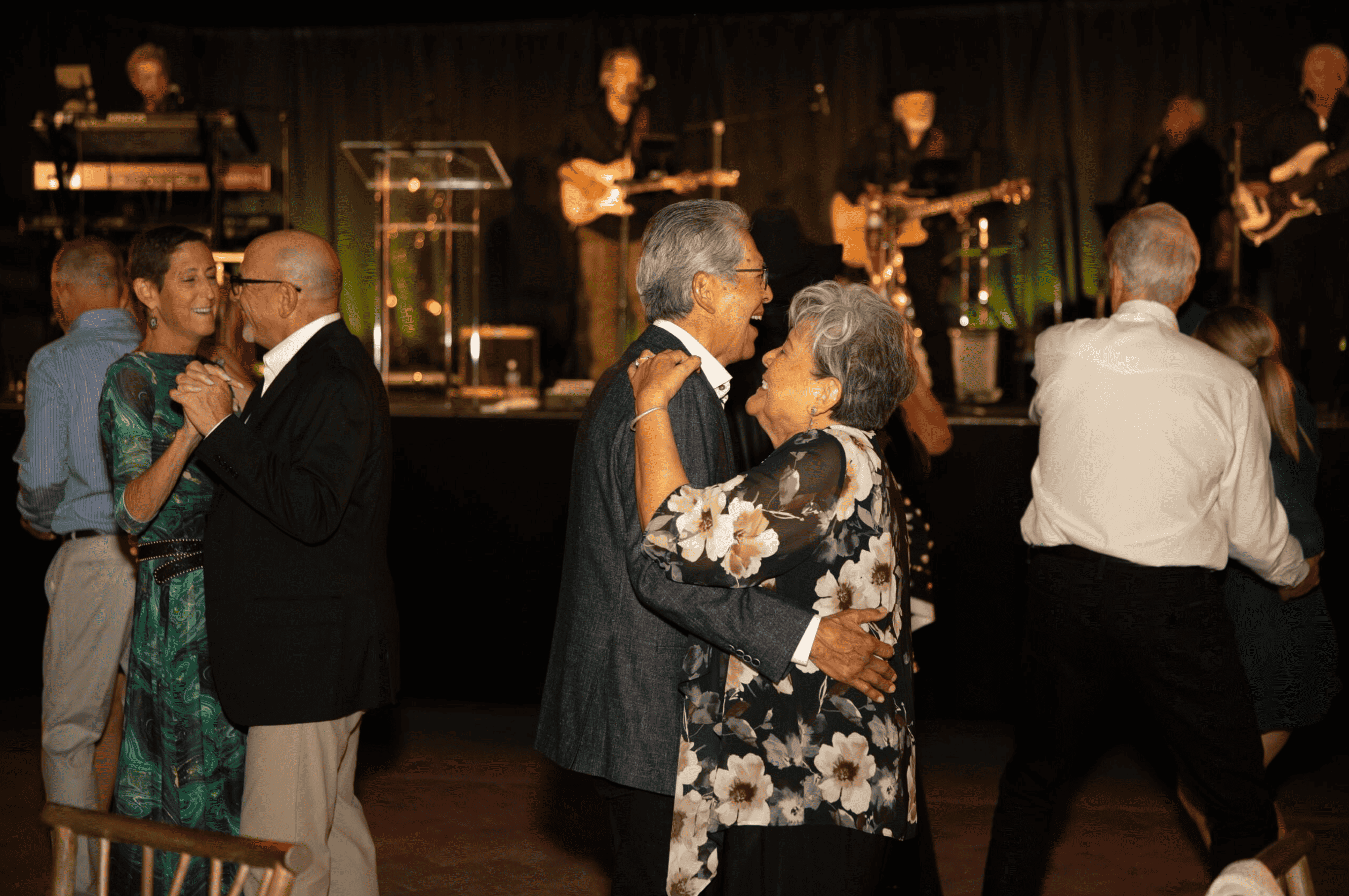 Couples dancing together at a ballroom event with a live band playing "Moondance" in the background.